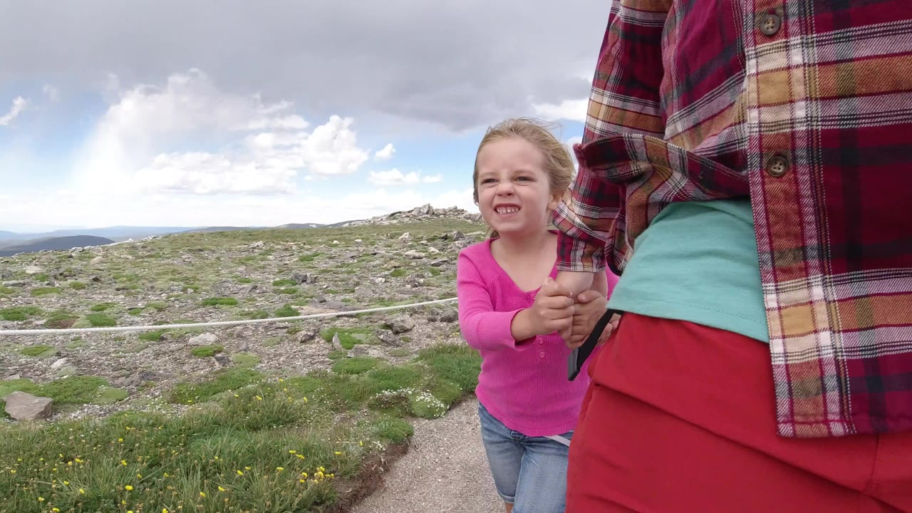 Young girl holding an adult's hand on a rocky mountain trail.
