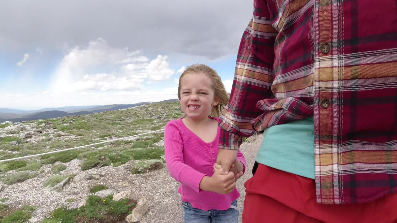 Young girl holding an adult's hand on a rocky mountain path.