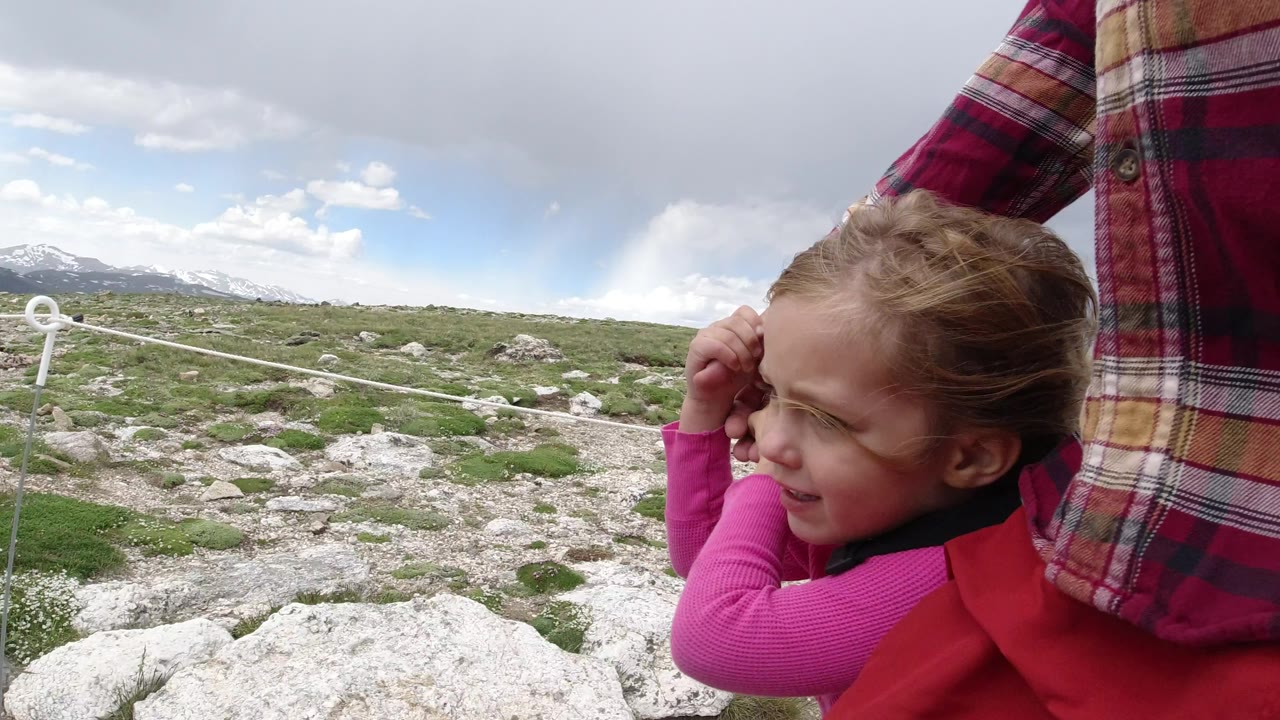 The girl remains close to the adult's side on the Winter Park trail, with her hand near her face, pale rocks in the foreground, and mountains stretching across the background.