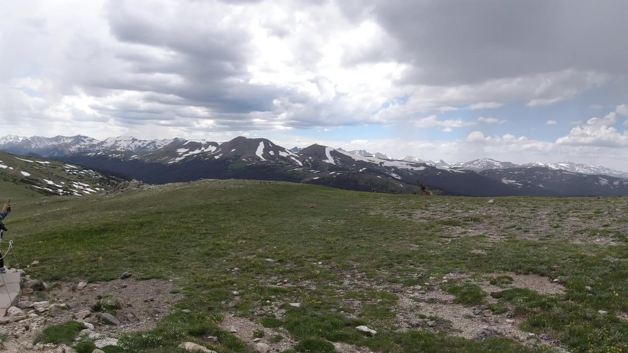 Wide grassy ridge with distant snow-streaked mountains under clouds