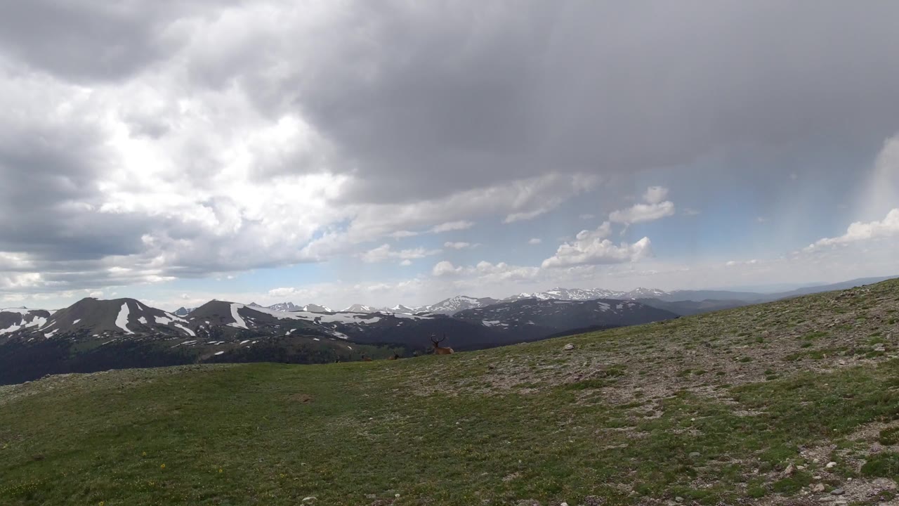 Wide Winter Park, Colorado mountain view with grassy foreground, distant snow-streaked ridges, large gray clouds, and no visible people.