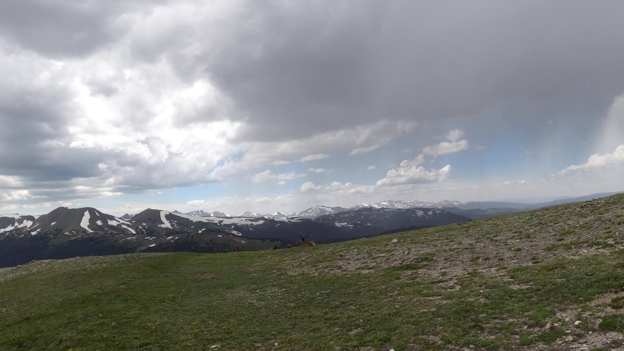 Winter Park, Colorado landscape with a rocky green slope rising at right, layered mountain ridges across the horizon, heavy cloud cover, and no visible people.