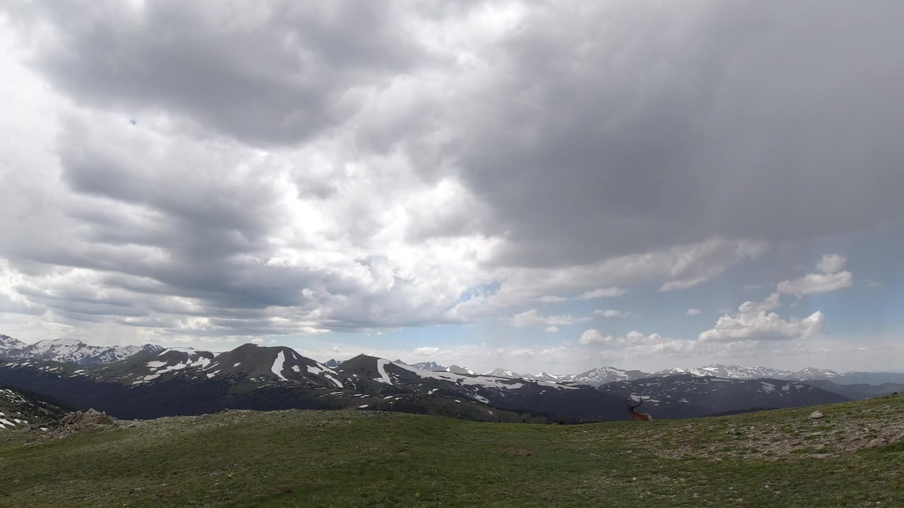 Winter Park, Colorado mountain view with a rolling grass foreground, dark ridgelines, patchy snow, layered storm clouds, and no visible people.