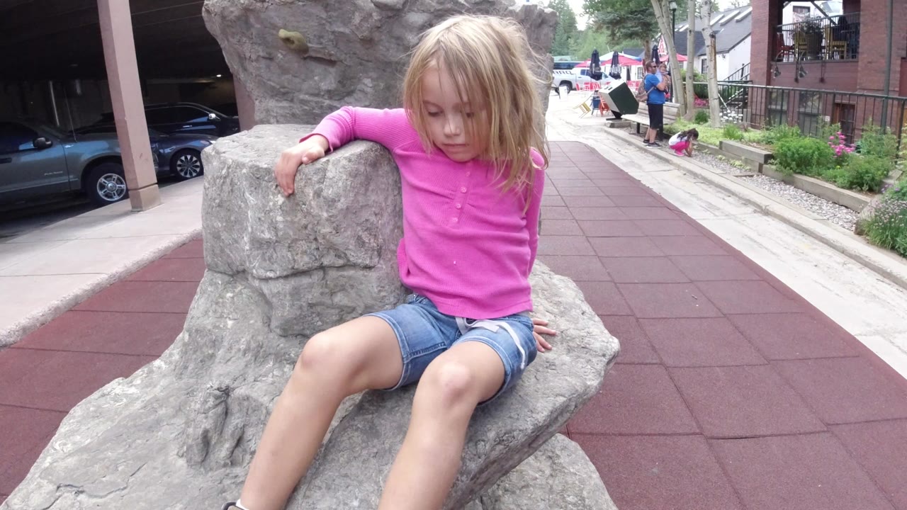 Young girl sitting on a gray play rock beside red rubber paving.
