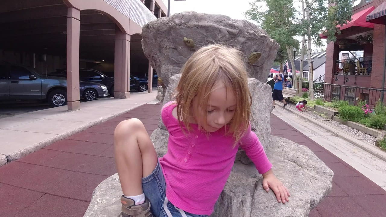Young girl in pink climbing on gray rocks beside a red walkway.