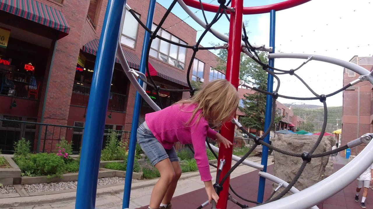 Young girl climbing a rope play structure beside red and blue posts.