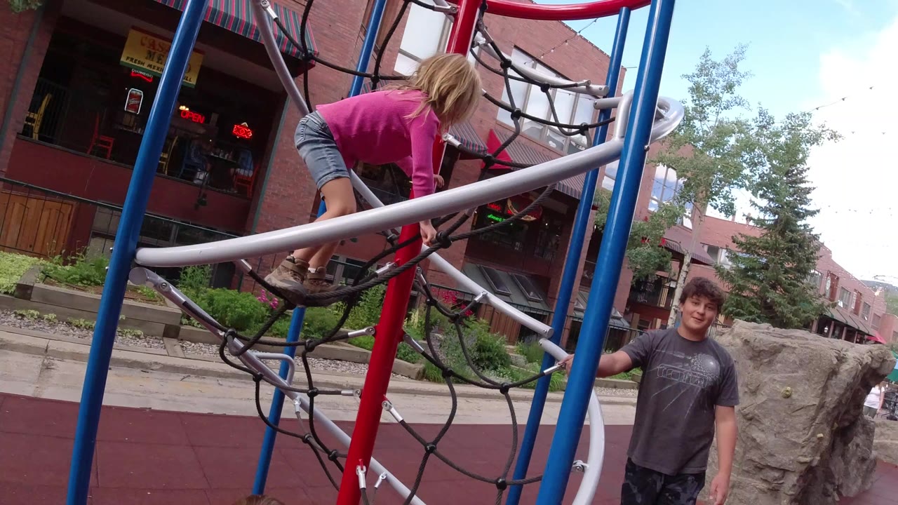 Girl climbing playground ropes with adult man beside the structure.