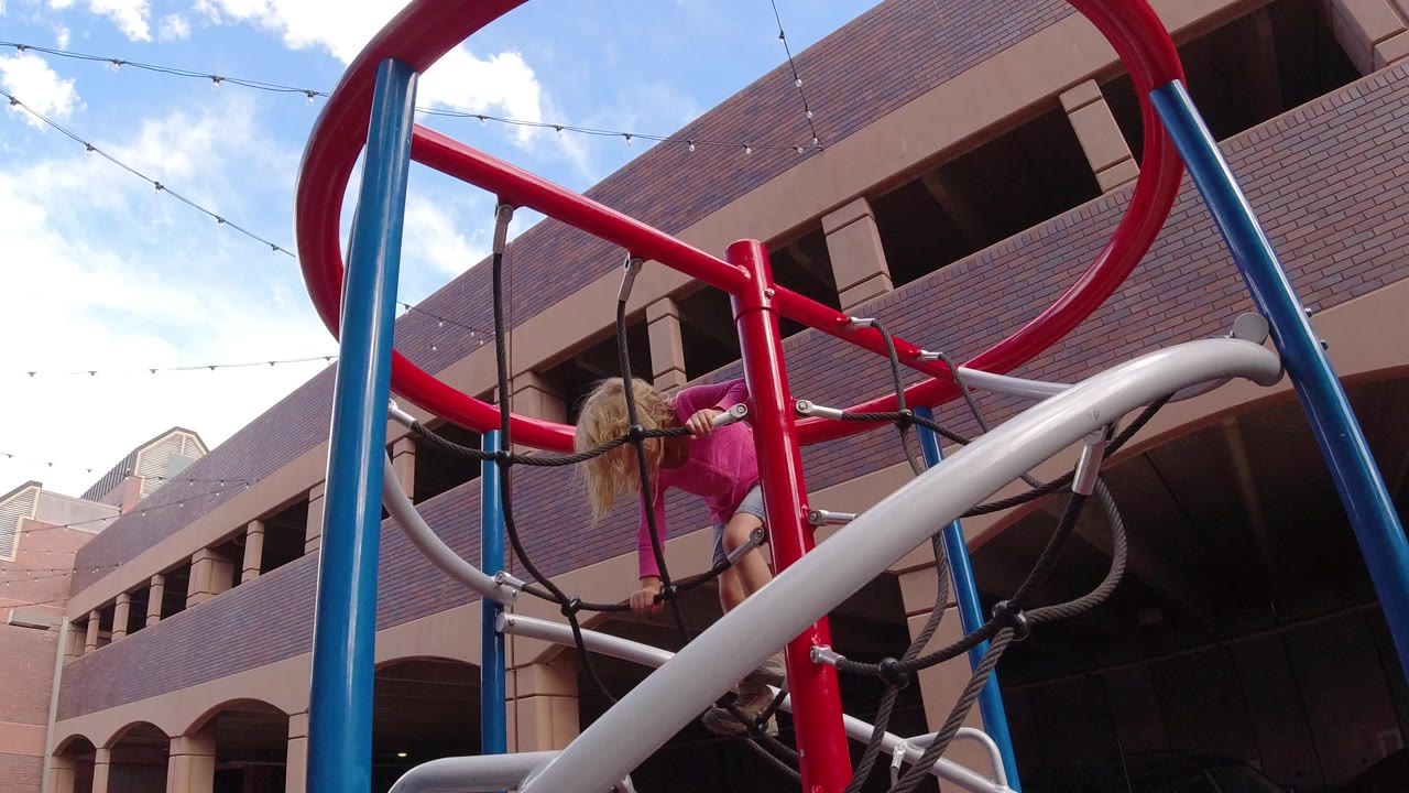 Child climbing red and blue playground structure beside brick building.