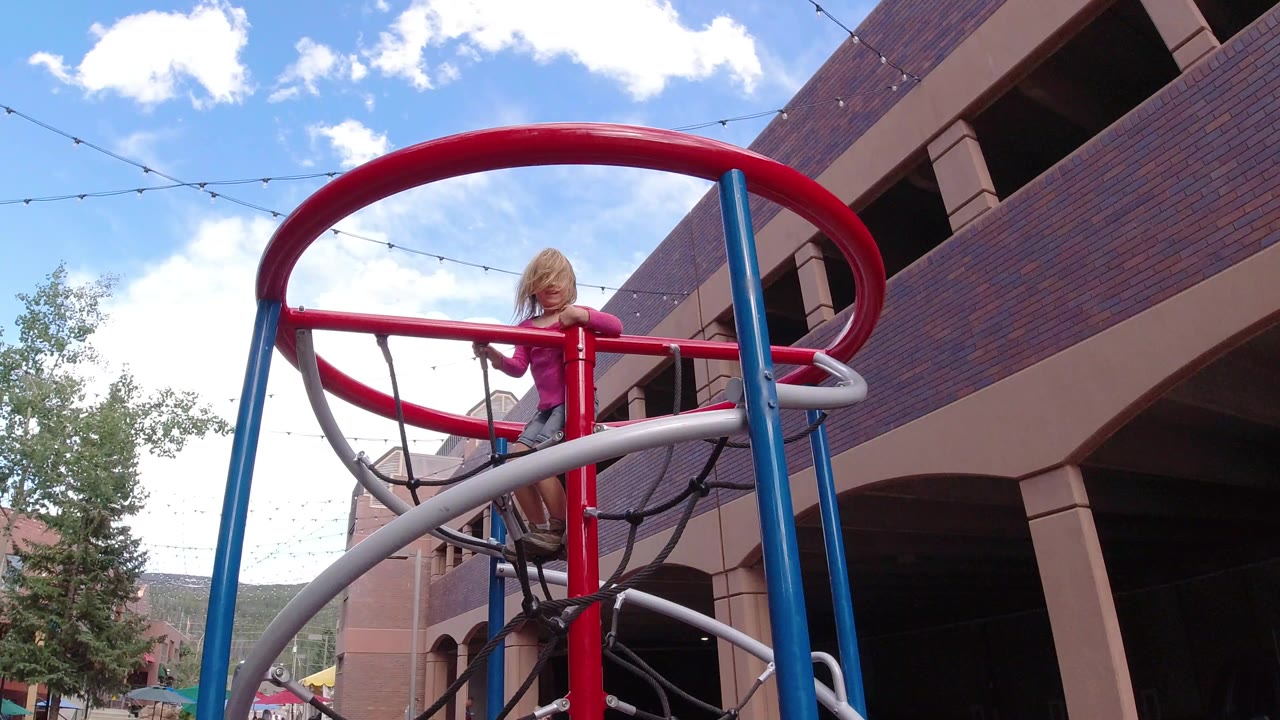 Young girl standing at the top of a red and blue jungle gym.