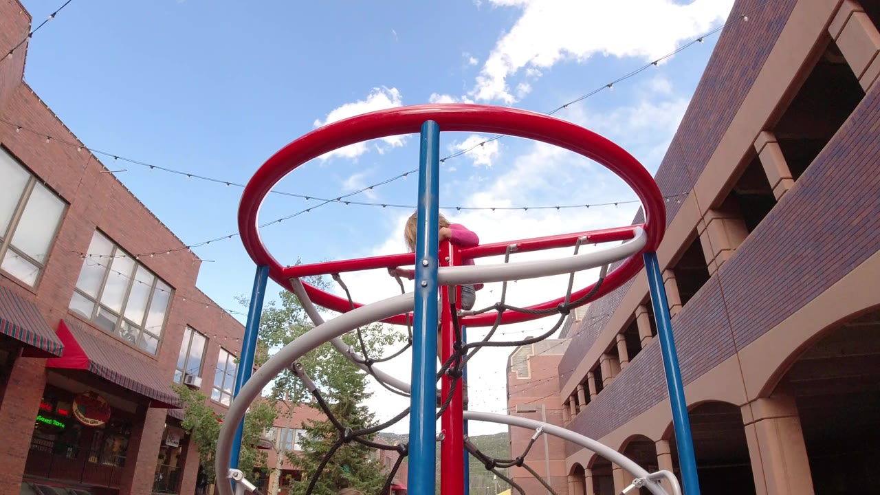 The child remains high inside the red circular play structure in Winter Park, Colorado, with the blue support post cutting through the center of the frame.