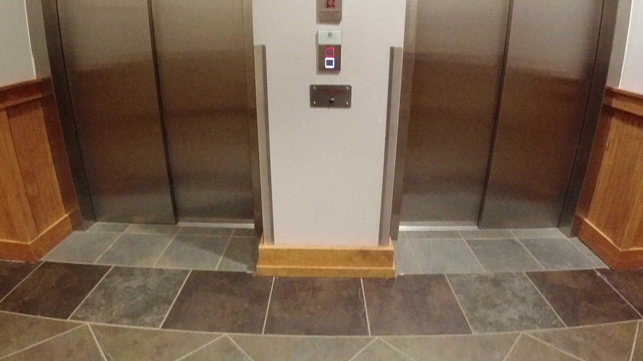 Closed stainless elevator doors in a Winter Park, Colorado interior, with a call panel on the wall, gray tile flooring, warm wood trim, and no visible people.