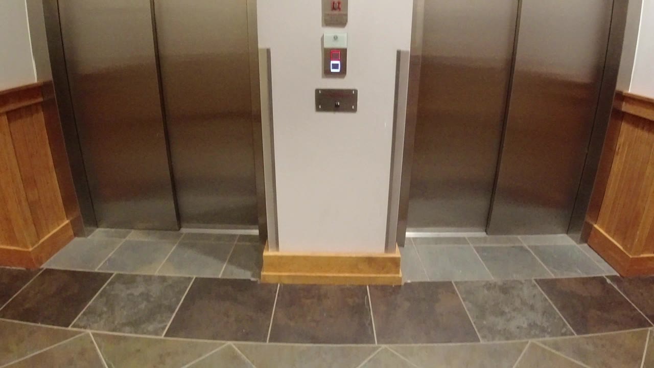 A slightly shifted view of the Winter Park elevator bank shows the central white wall, stacked call controls, gray floor tiles, wood wall trim, and no visible people.