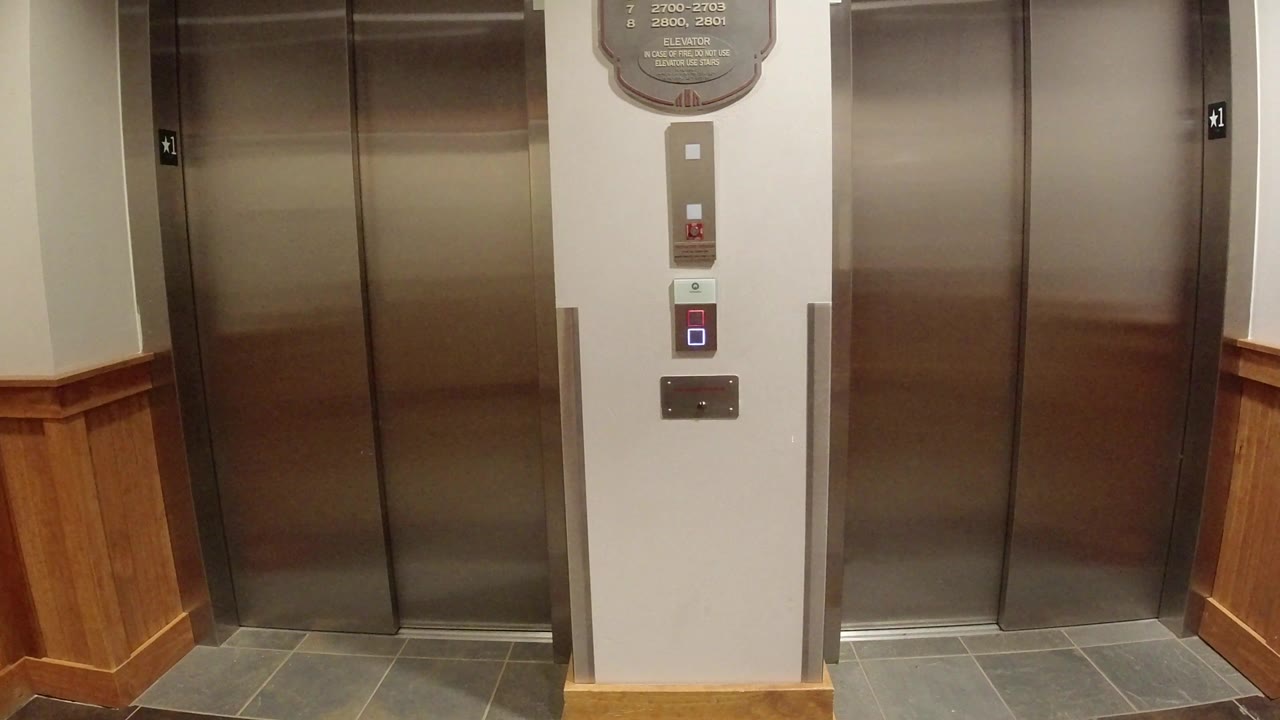 Winter Park, Colorado elevator bank framed straight on, showing brushed doors, call panel, wood wainscoting, gray floor tile, and no visible people.