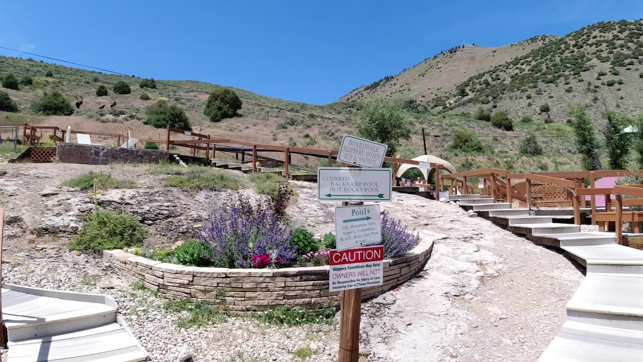 Mountain path with posted signs, wood railings, flowers, and dry hillside