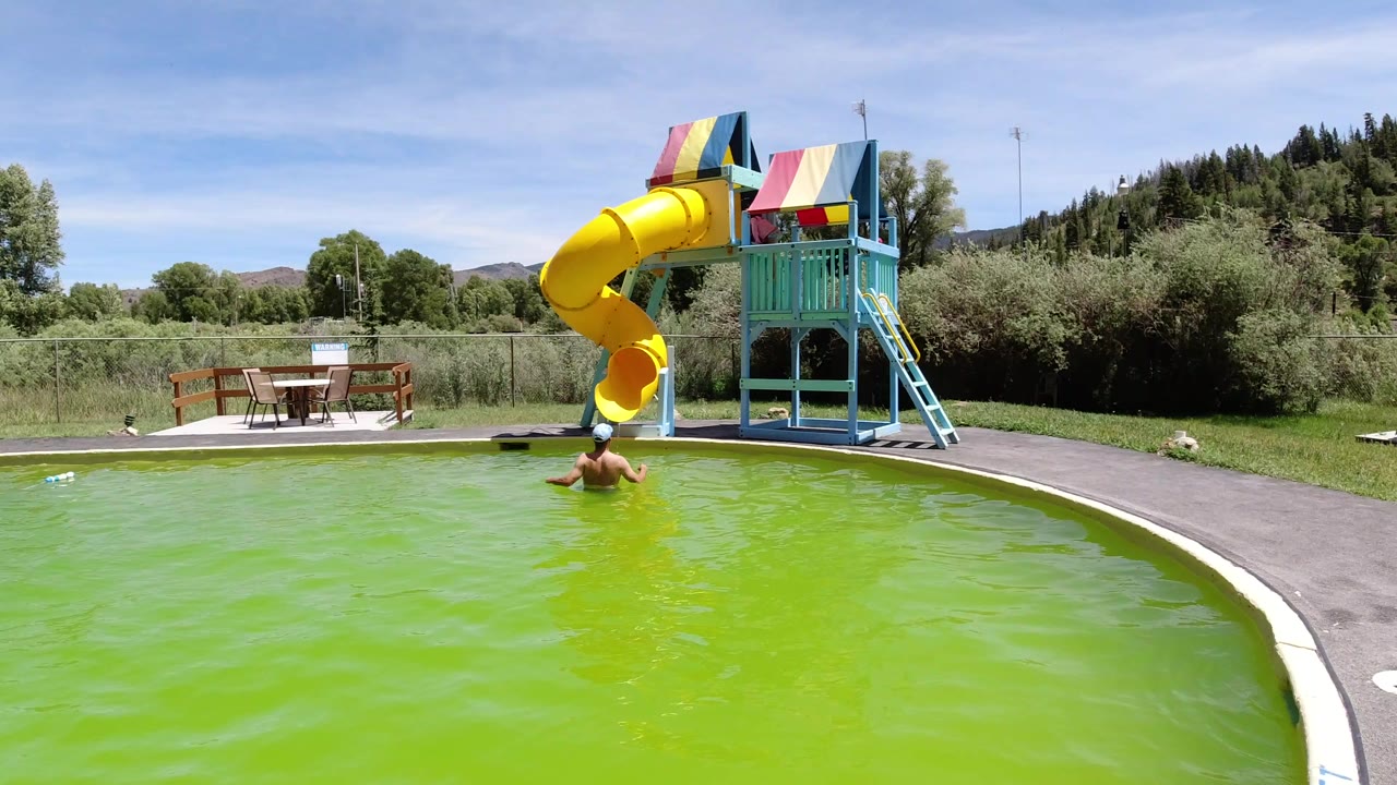 Man in a green pool facing a yellow tube slide