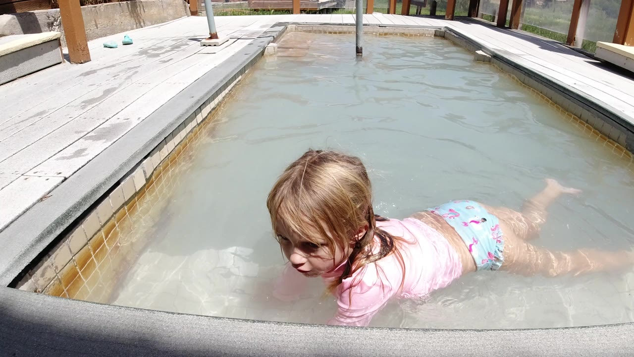 Young girl floating in a small outdoor pool beside a wet deck.