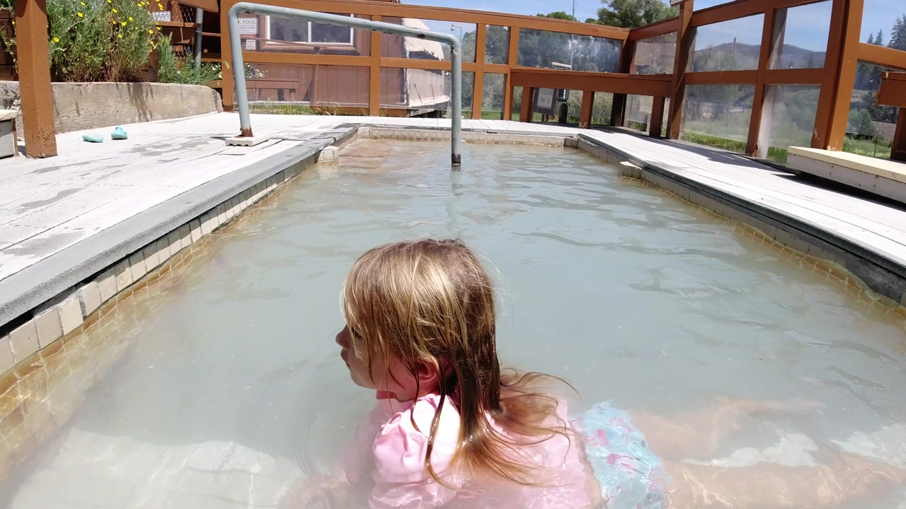 One second in, the blond child remains turned left in the Winter Park, Colorado pool, with rippled water, a metal handrail, and sunlit deck boards in view.