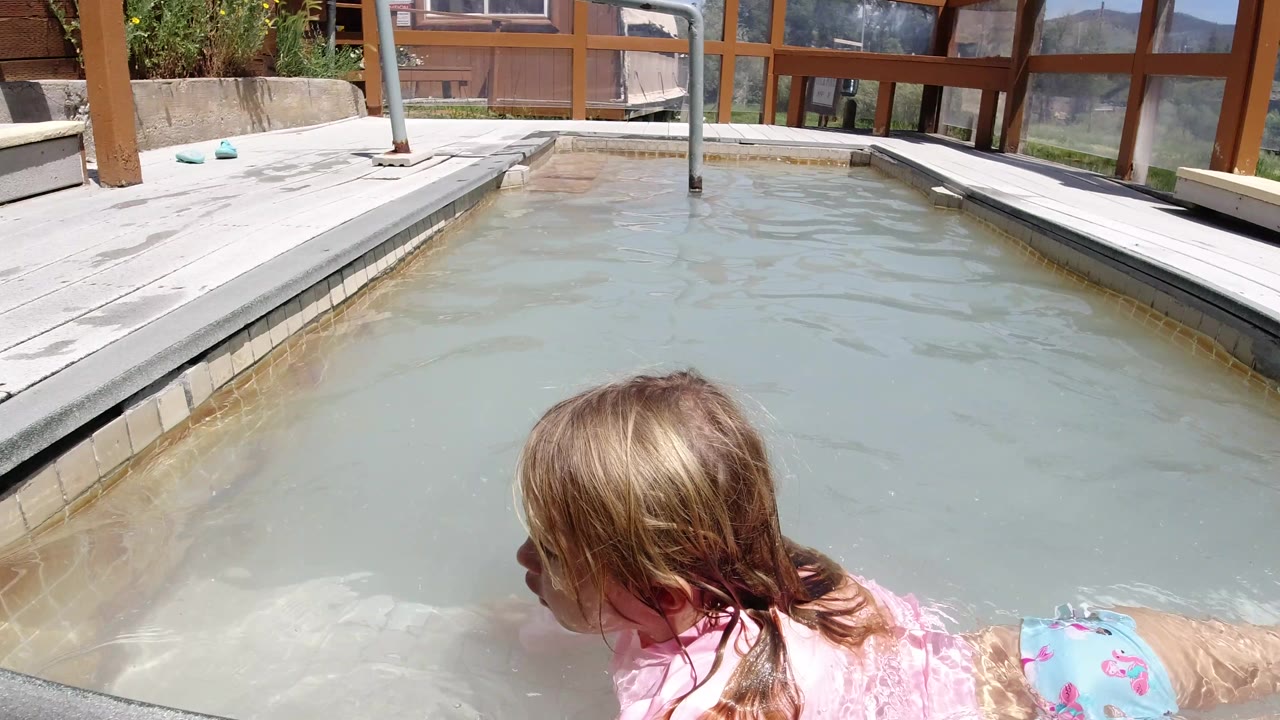 Child floating beside the pool edge in bright sun