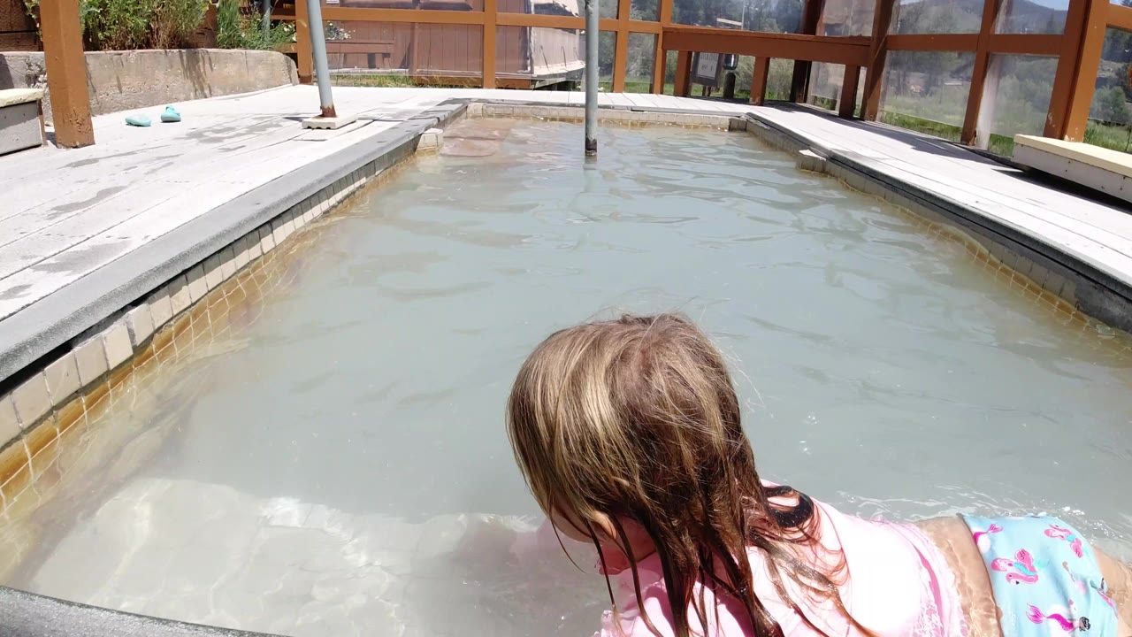 Young girl leaning over a shallow pool step in bright sun.