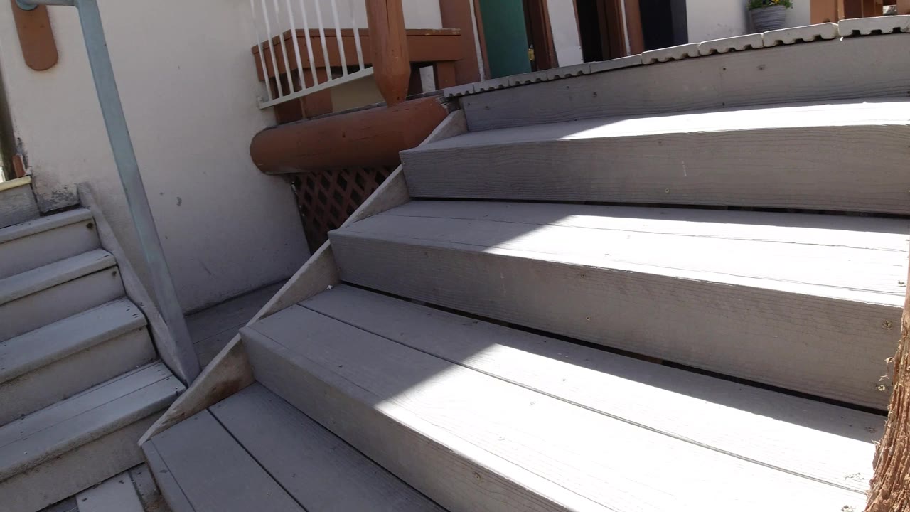 The stairs and upper deck fill the frame, with a white railing, wood posts, building trim, and sharp sunlight on the gray boards in Winter Park, Colorado.