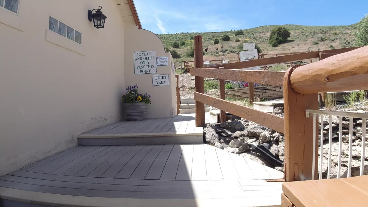 A deck corner beside a pale building shows a wooden rail, posted age and quiet-area signs, rocks, and a dry hillside in Winter Park, Colorado, with no visible people.