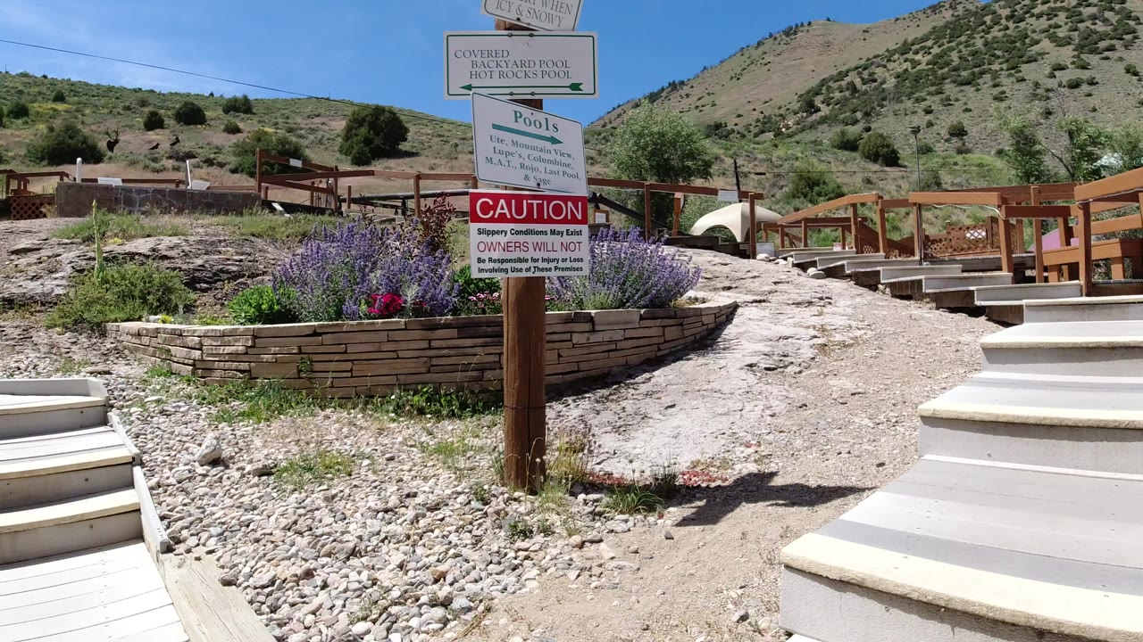 Hot pool and caution signs beside a mountain walkway.