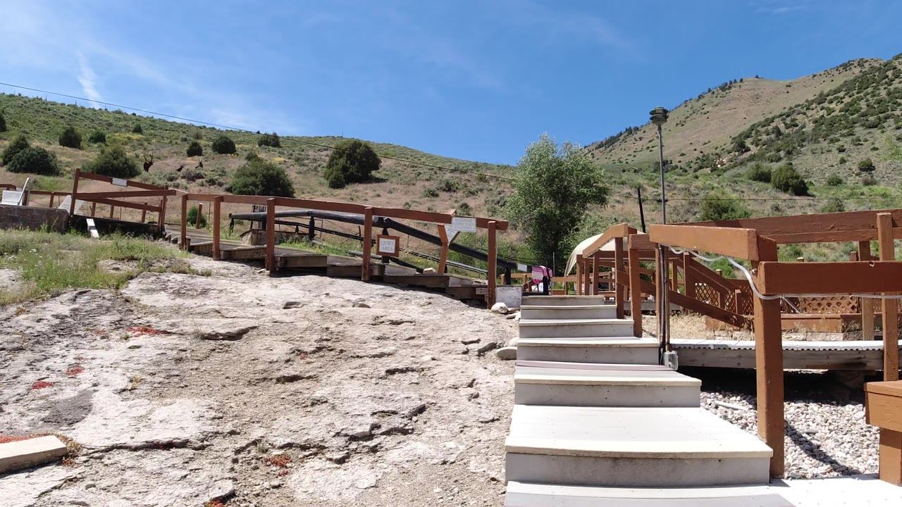 Wooden footbridge and stairs across dry rocky ground with hillside behind.