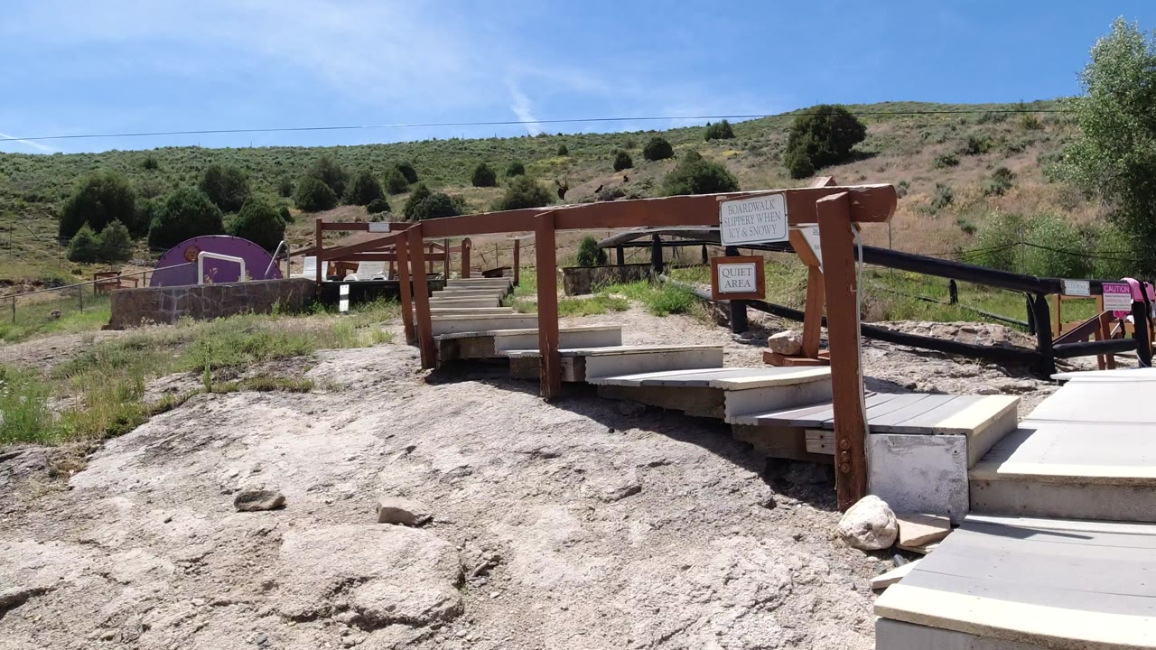 Sunlit boardwalk steps with wooden posts and hillside beyond.