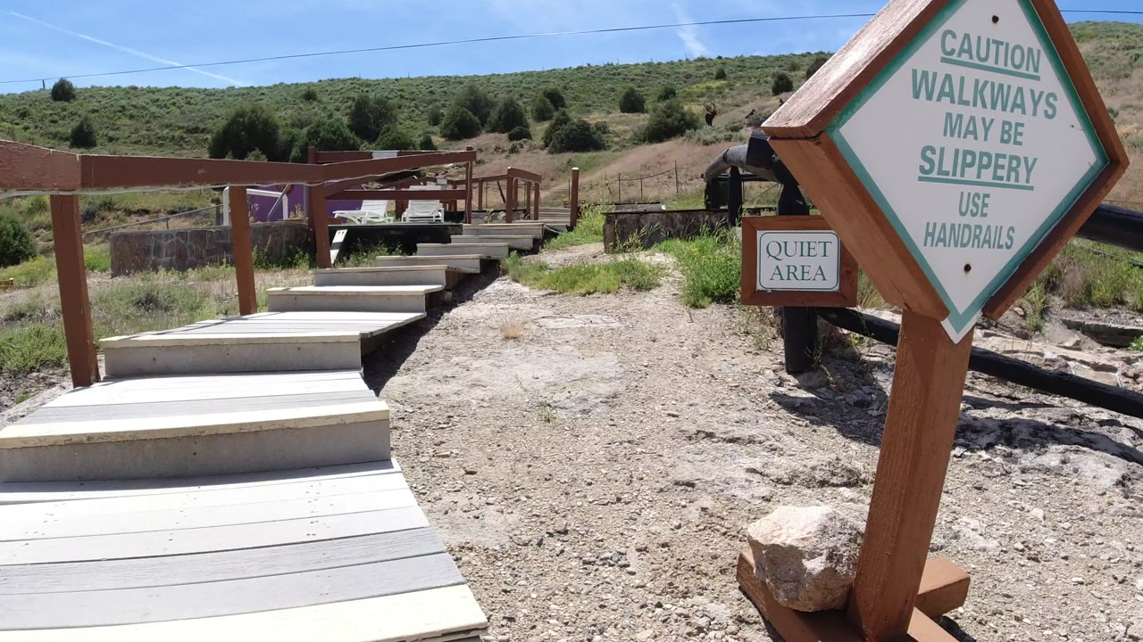 The walkway steps lead forward between brown rails toward a small platform area in Winter Park, Colorado, with dry ground, green brush, and no visible people.