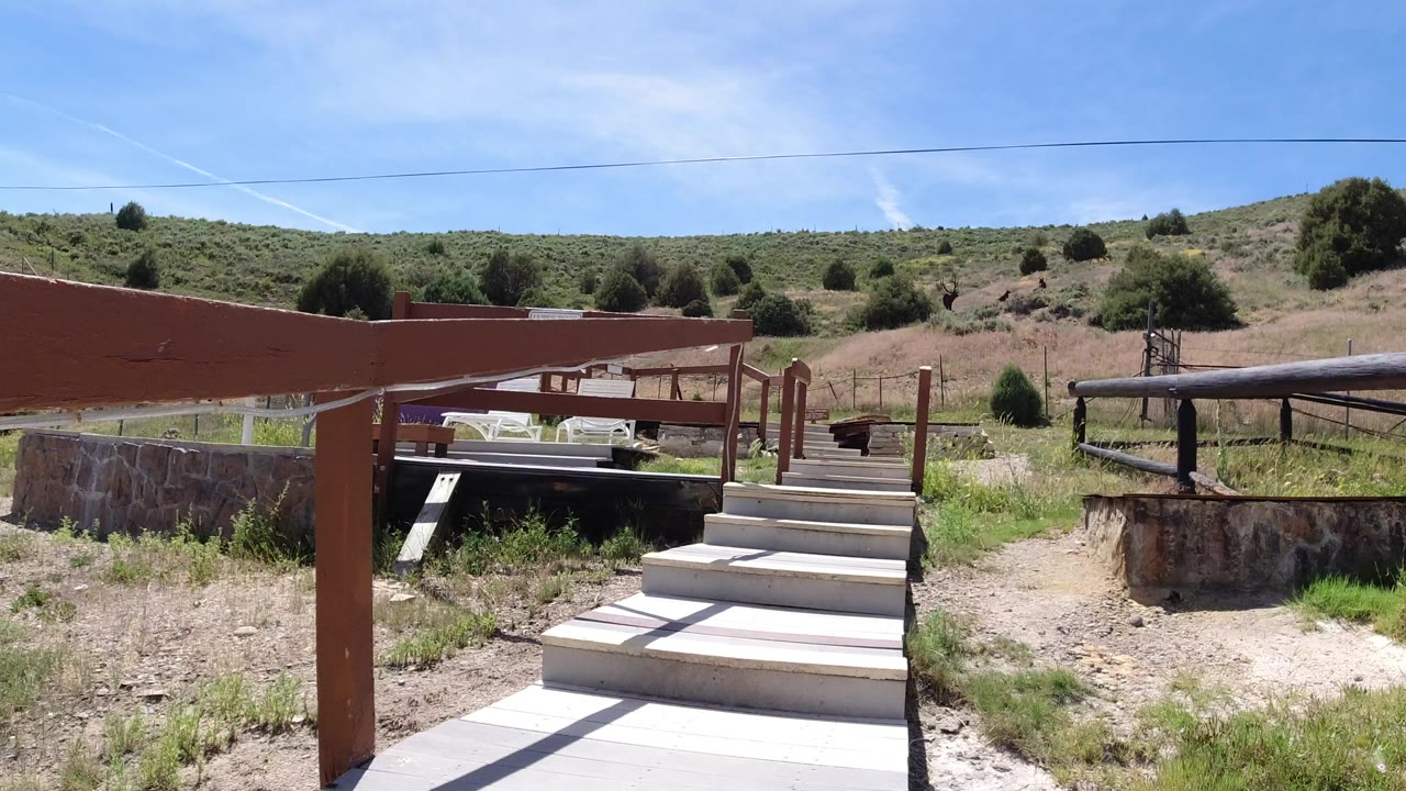 White deck steps leading toward a rural hillside under blue sky.