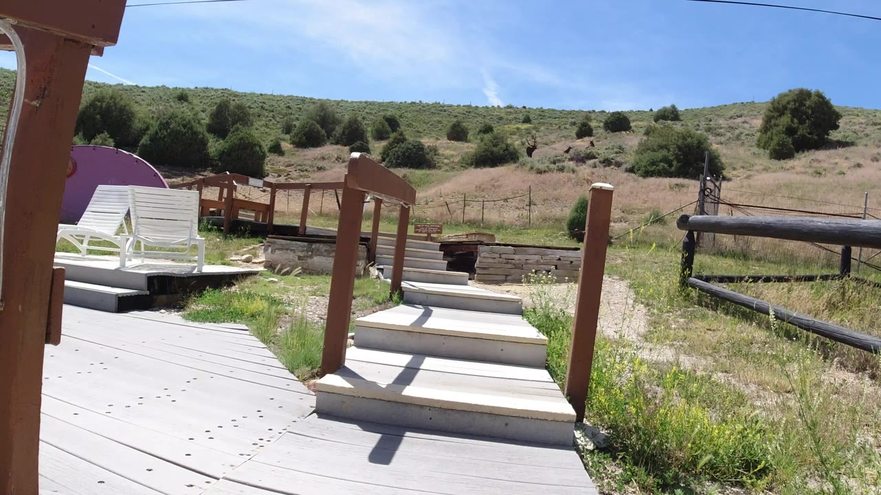 Winter Park, Colorado catwalk view with pale steps centered between brown posts, lounge chairs to the left, a fenced hillside beyond, and no visible people.