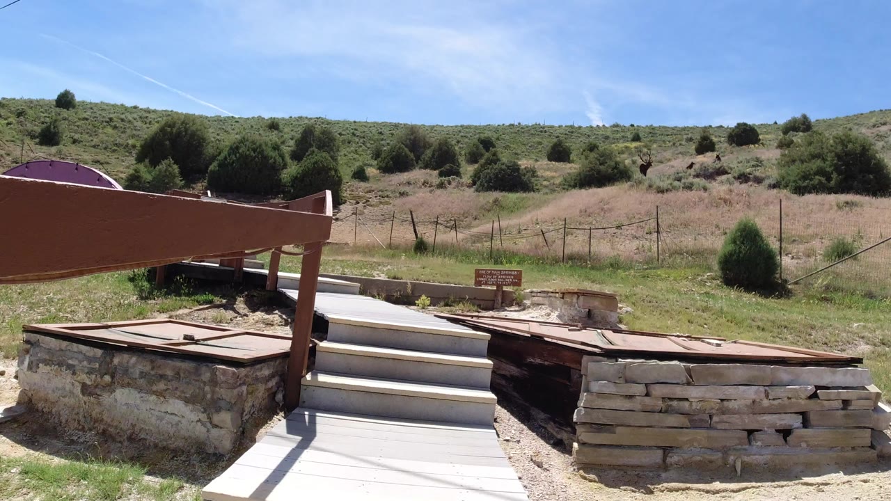 Wooden catwalk and steps beside stone walls under a sunny hillside.
