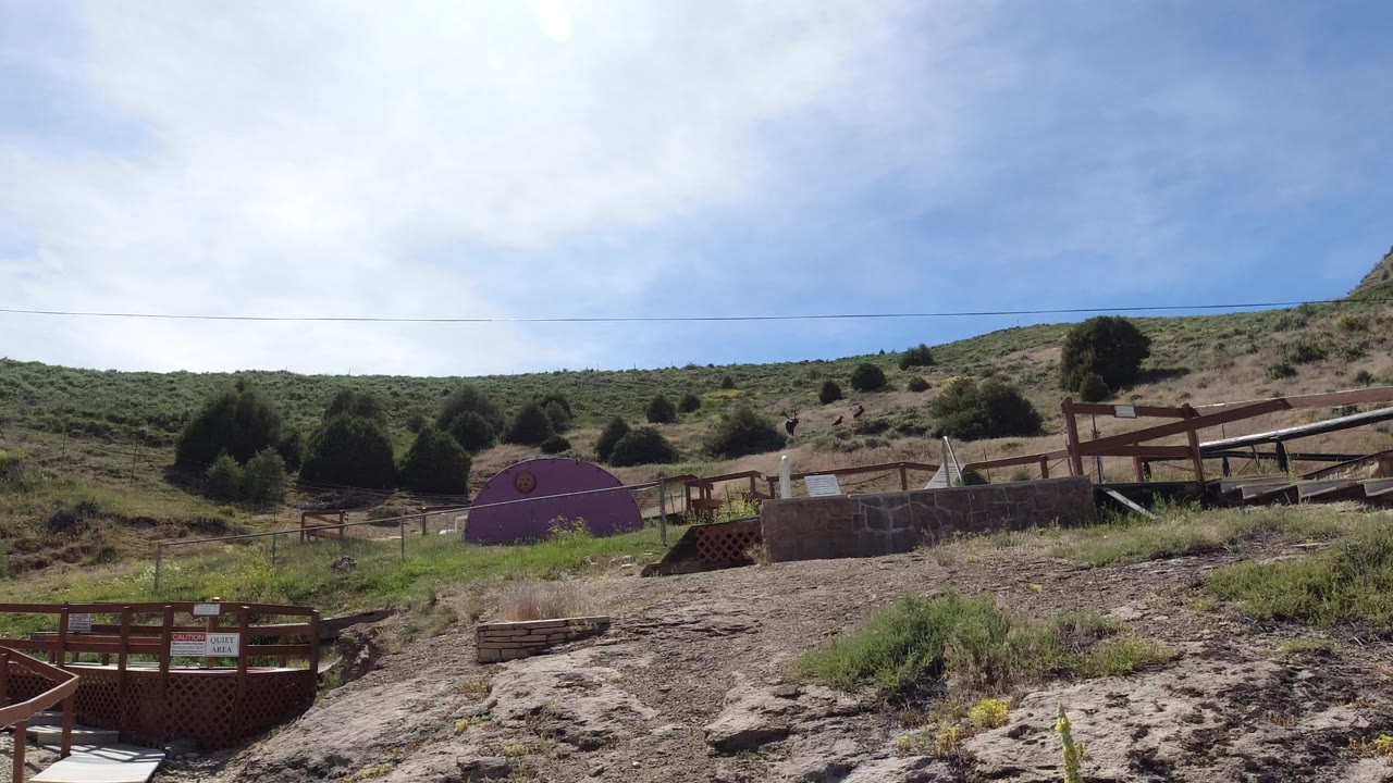 Wide Winter Park, Colorado hillside view with rocky ground, wooden railings, a purple dome-like structure, scrub vegetation, blue sky, and no recognizable people.