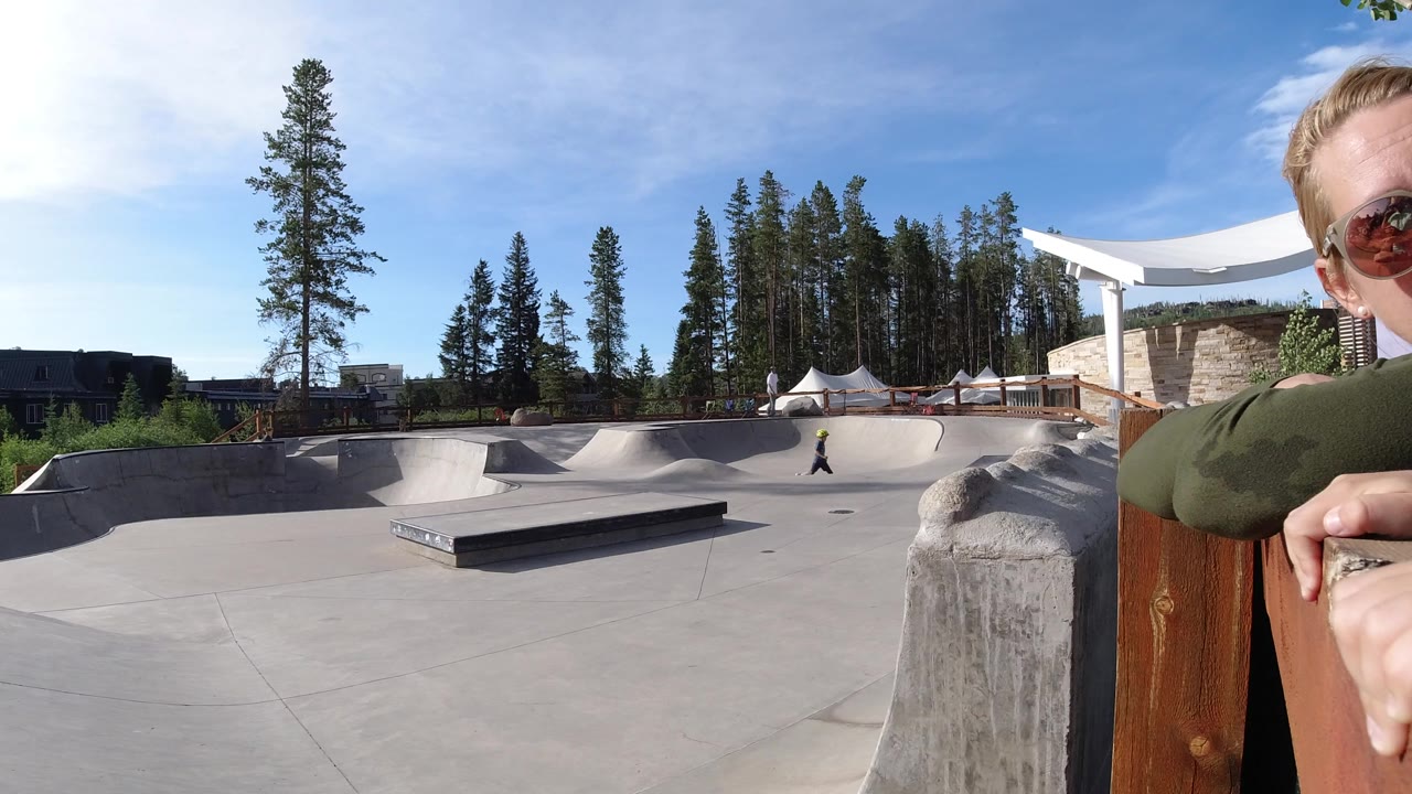 Wide skatepark view with a partial adult face at the right edge.