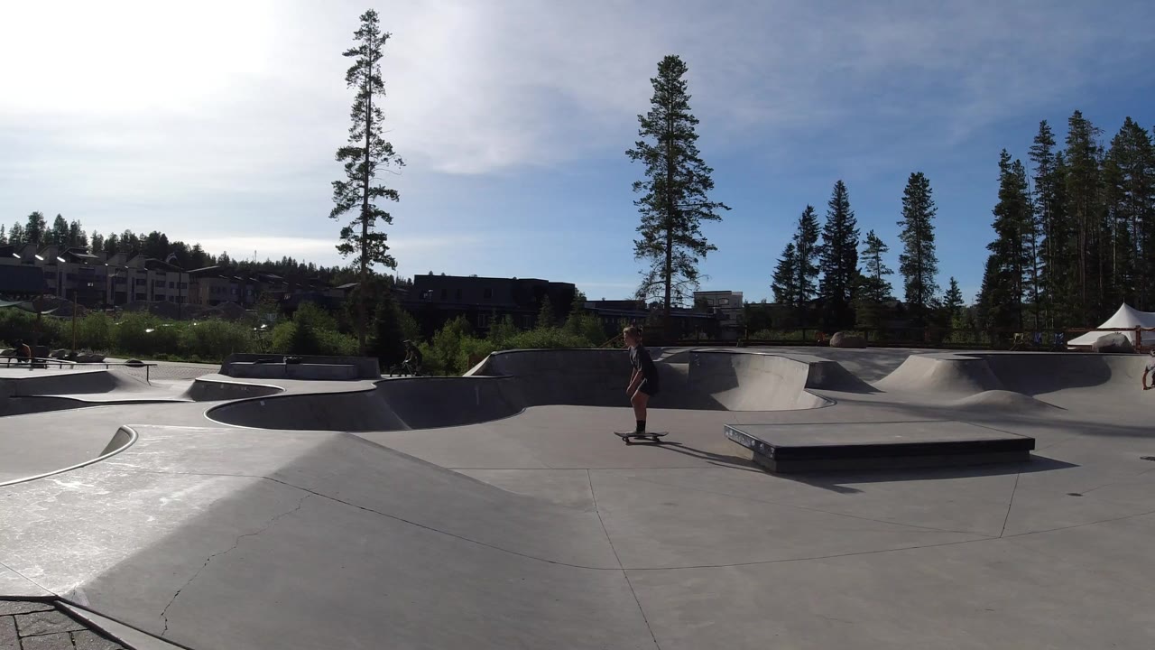Wide sunny skate park with skater near concrete ramps
