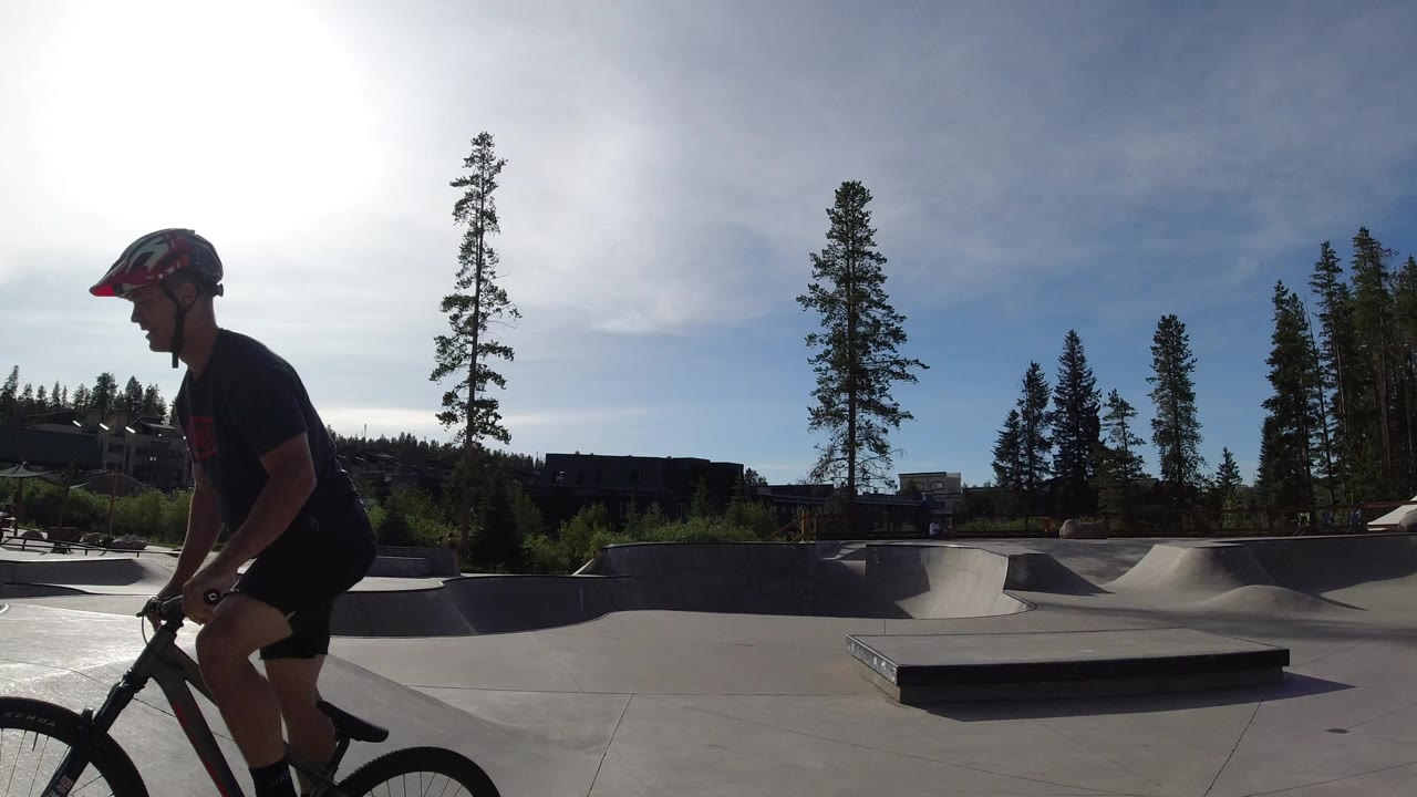 Cyclist passing close to camera at a sunlit concrete skate park.