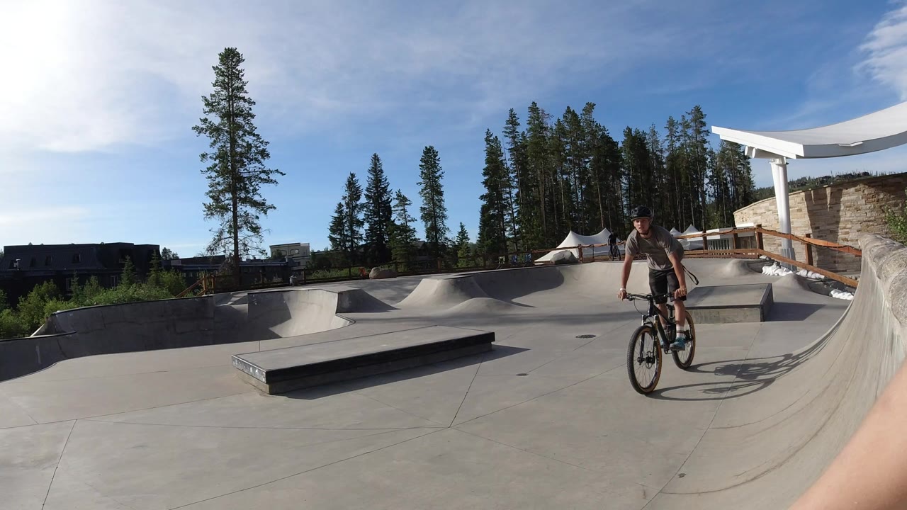 Boy riding a bicycle across a concrete skatepark under bright sun.