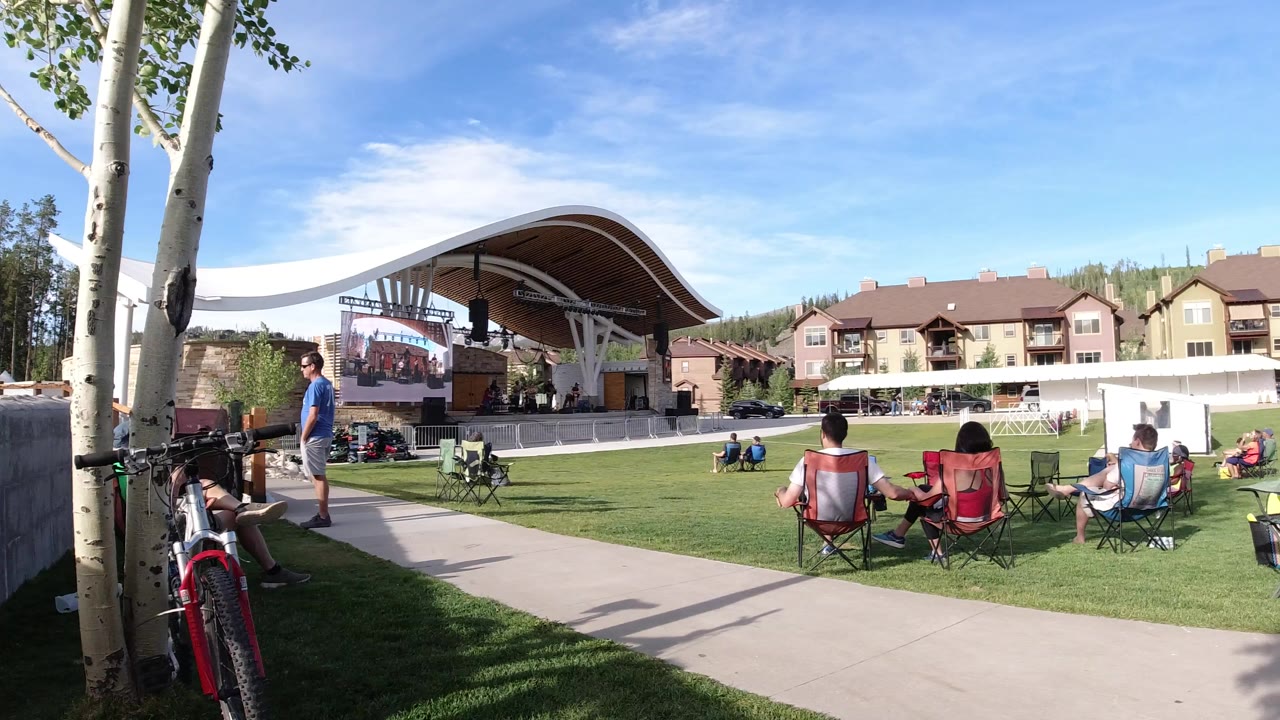 Outdoor lawn audience facing a covered stage with bicycles near trees