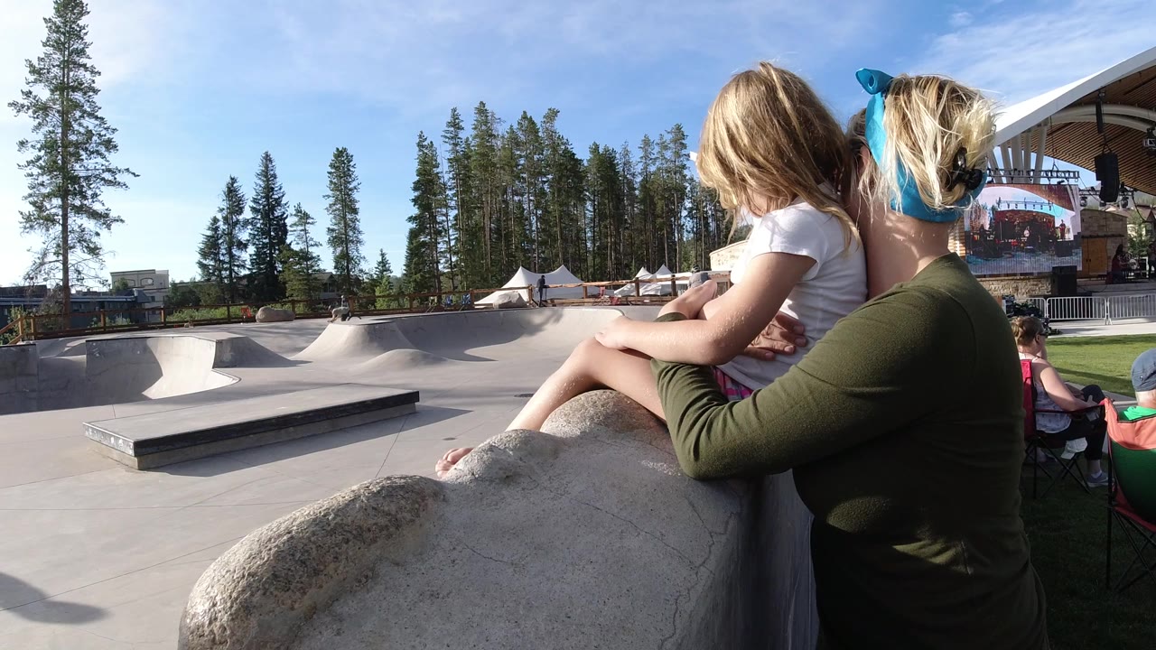 Woman holding a young girl beside a skatepark in bright daylight.