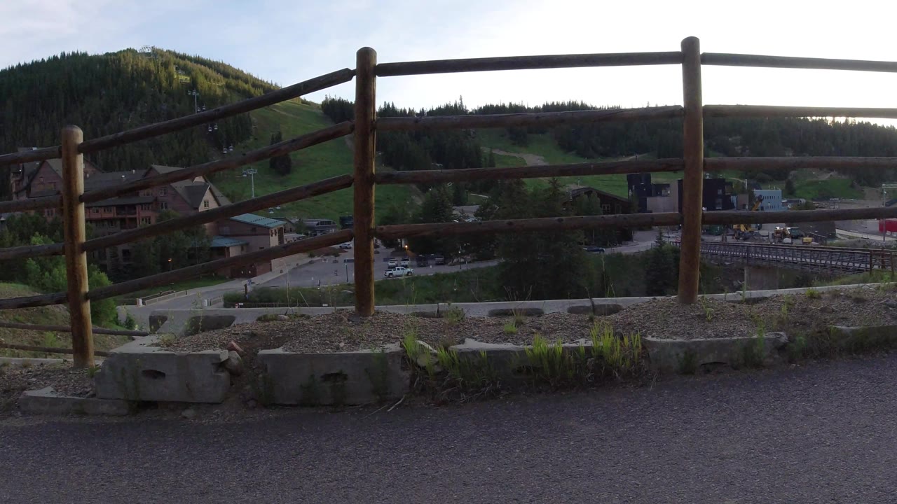 Foreground railing across a mountain base area with slopes, buildings, and forest.