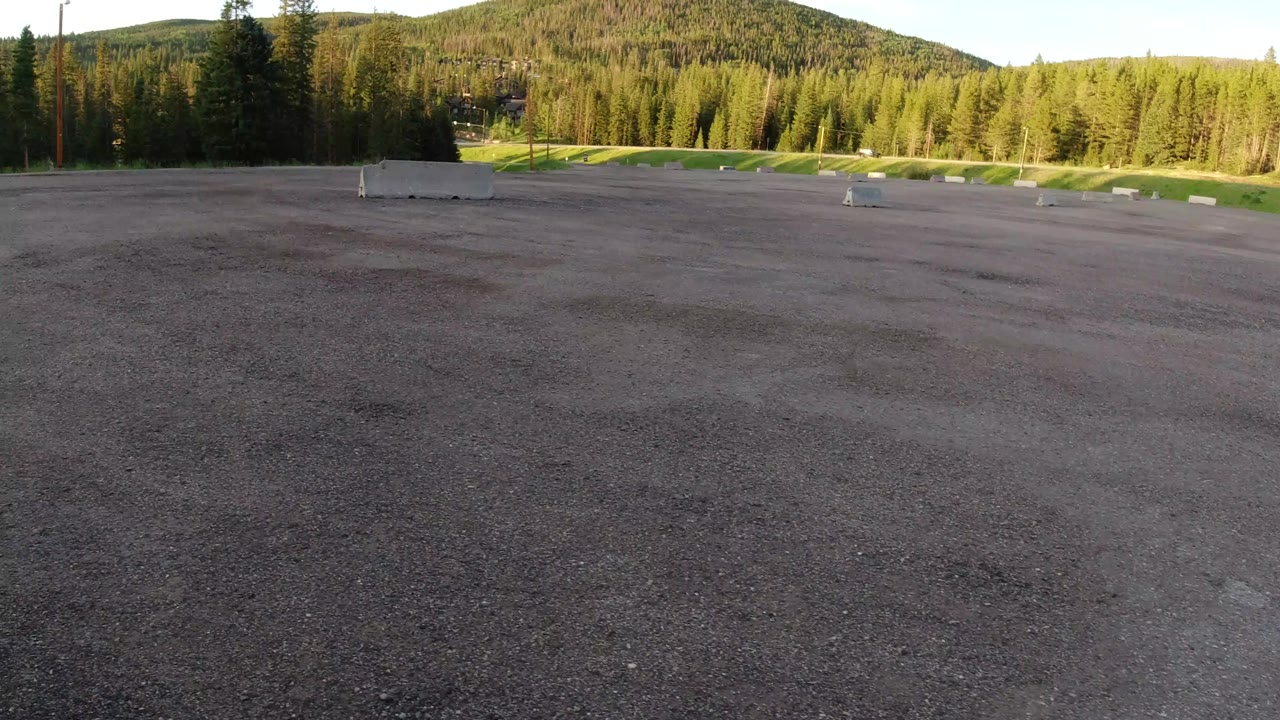The second frame keeps the Winter Park, Colorado clearing wide, with dark ground in front, scattered concrete barriers near the grass, and dense trees beyond, no visible people.