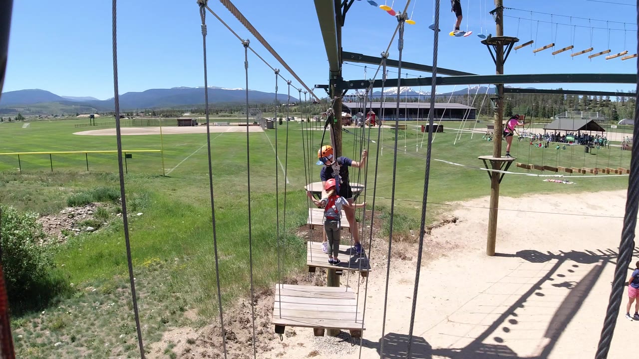 People wearing helmets on a ropes course platform above grass and dirt.