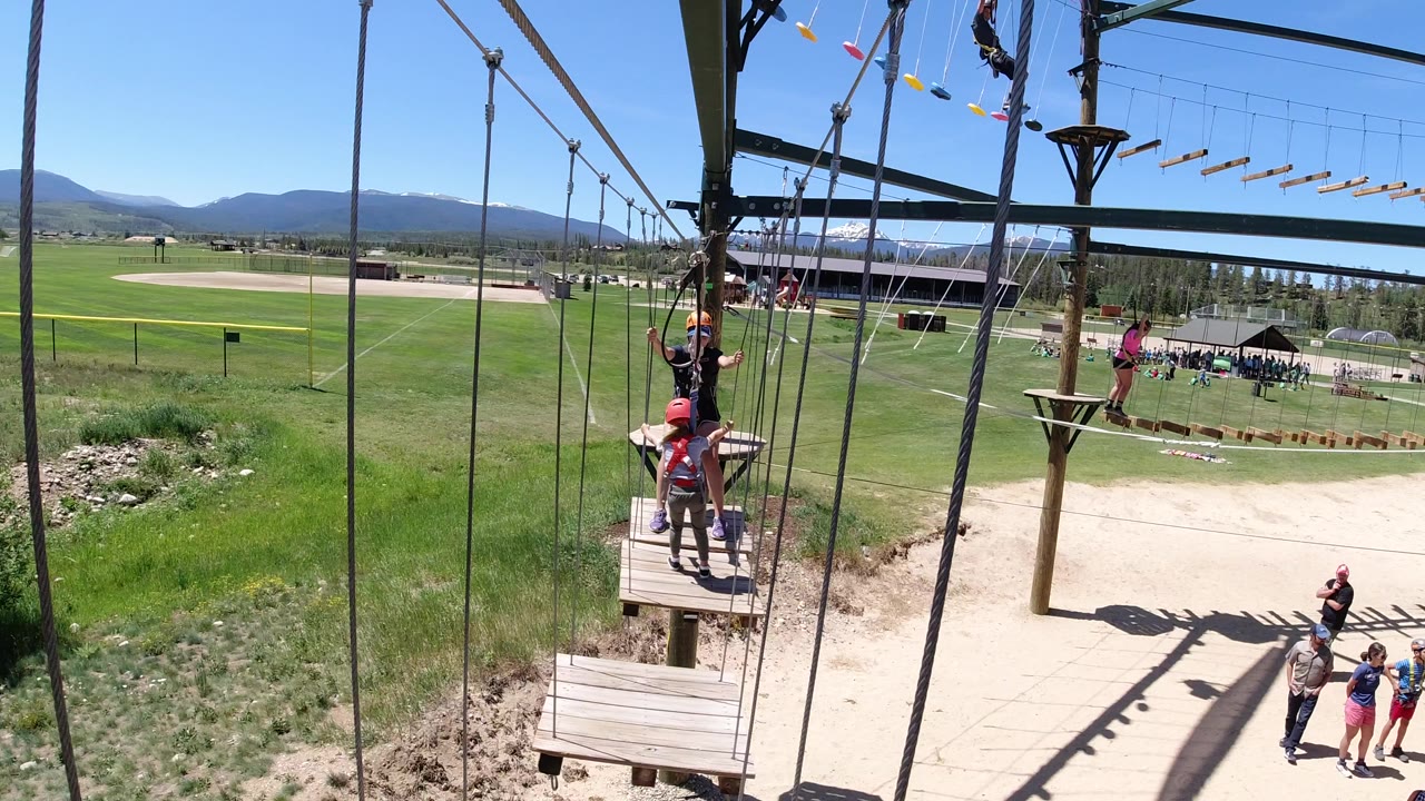 Children in helmets on a ropes course platform with mountains behind them.