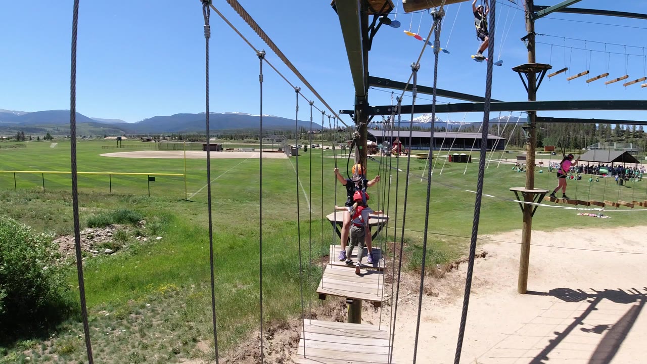 People on a ropes course platform above a grassy field.