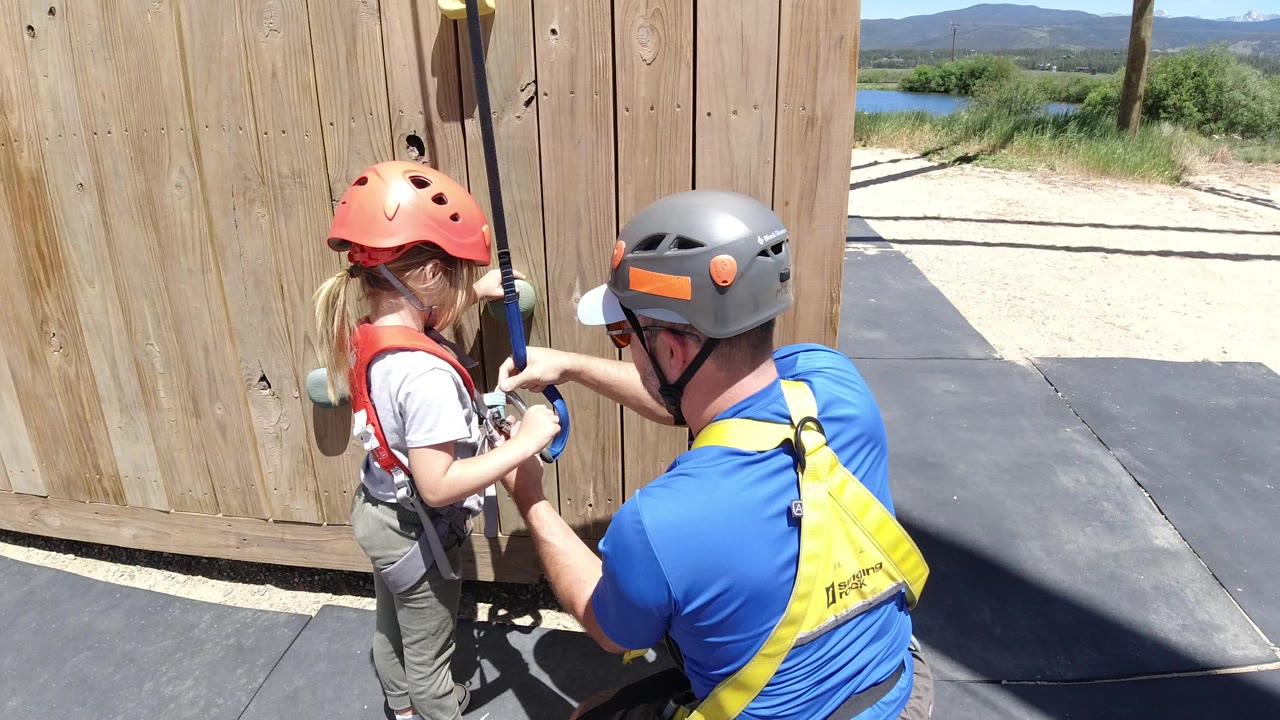Girl in climbing helmet with adult beside wooden wall