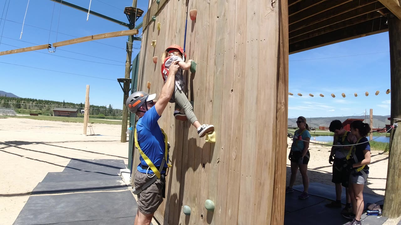 Father helping a young girl climb a wooden wall.
