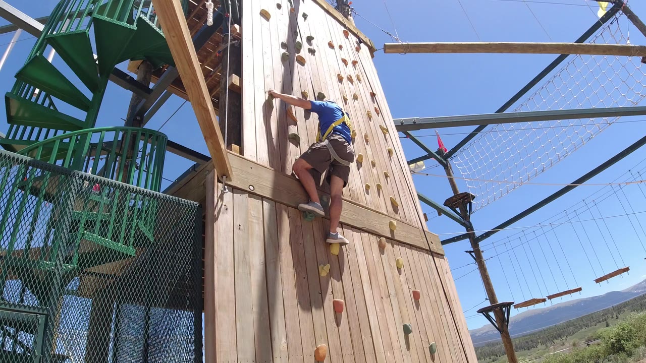 Man in a harness climbing a wooden outdoor wall