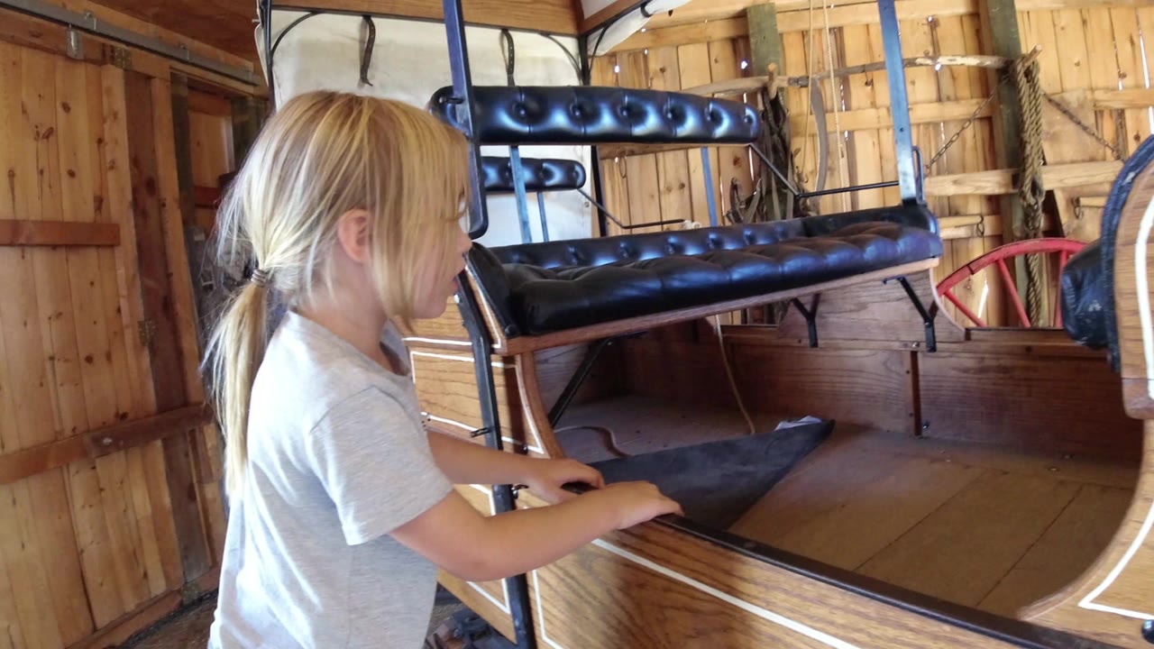 Blonde child beside a wooden boat-shaped chair inside a cabin.