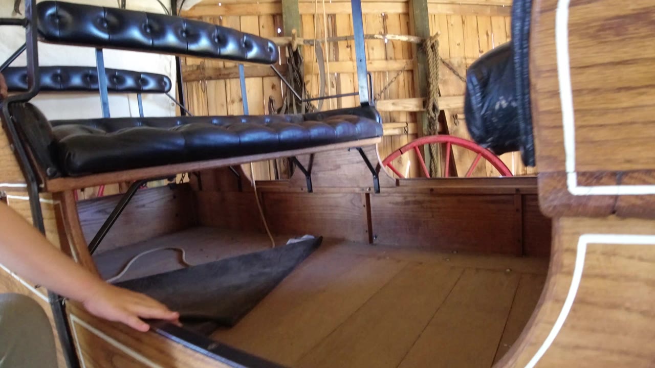 Wooden cart interior with black padded bench and a person reaching in.