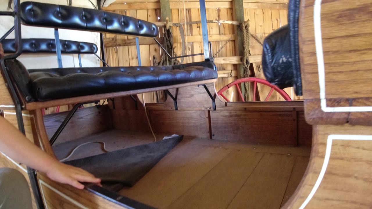 A close passenger-level view in the Winter Park, Colorado cart shows a hand near the wooden floor, black bench cushions, and red wheel spokes behind the side panel.